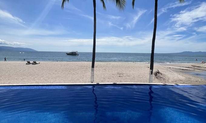 Infinity pool with two palm trees framing the white sand beach and Caribbean Sea